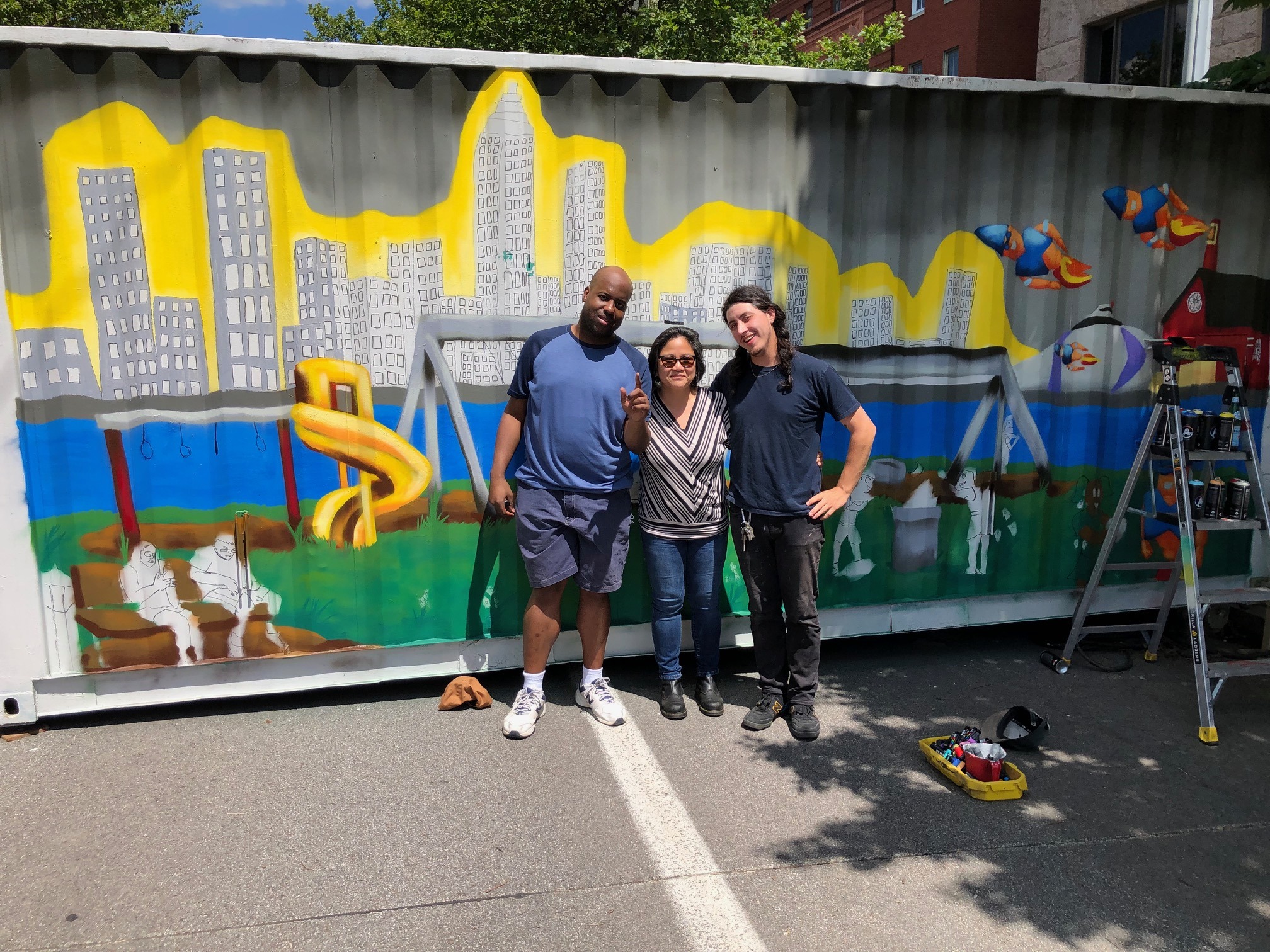Three artists, Matthew Carroll, Fran Ledonia Flaherty, and Max Gonzales in front of a mural painted on the side of a shipping container