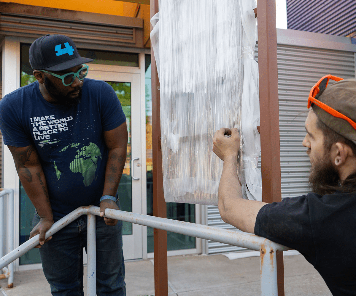 Two people, including artist Jason McKoy, are looking at a steel frame that has been installed in Sharpsburg. The frame is wrapped in a protective material.