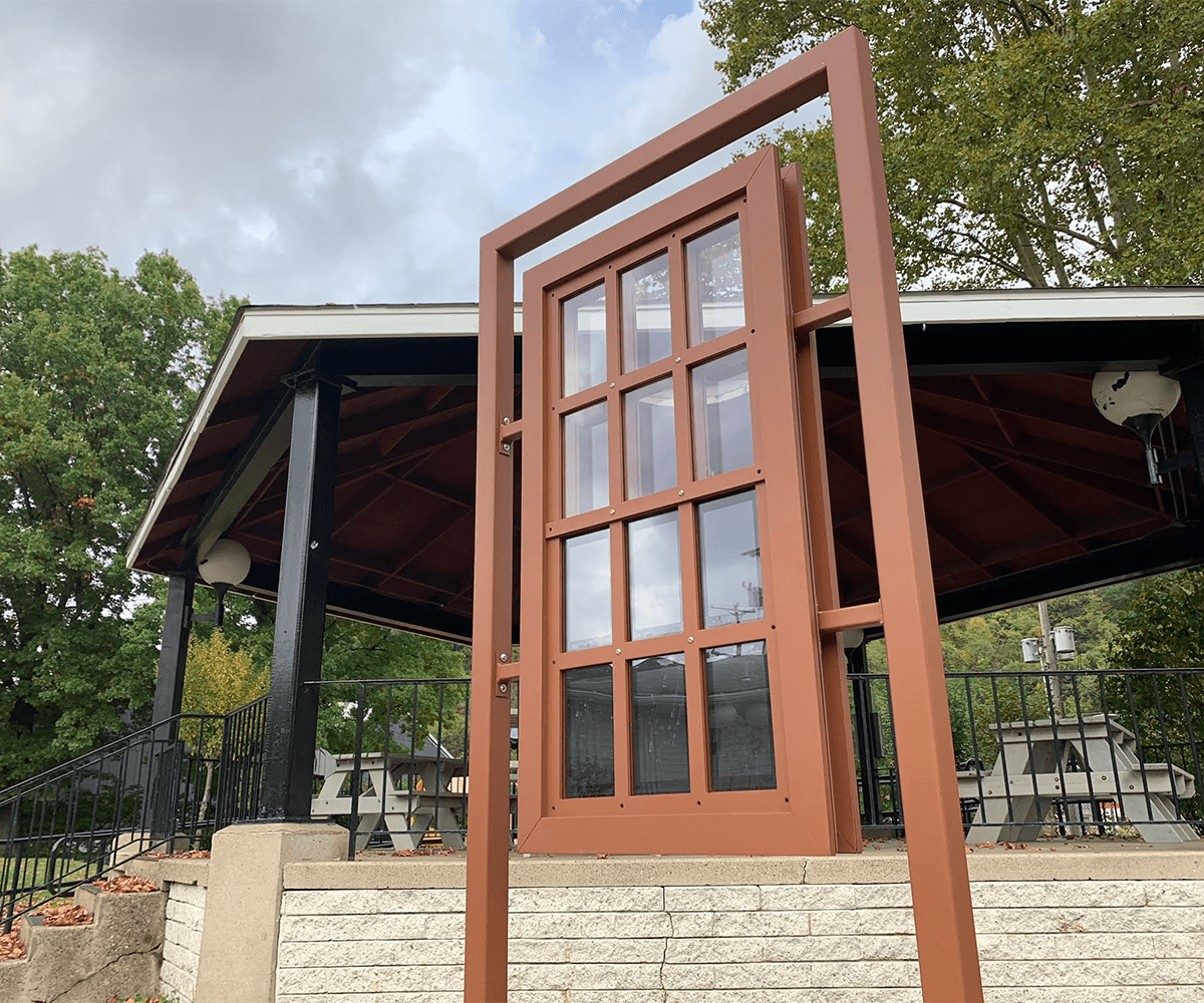 View of the We Are Windows installation in Etna. This is a light brown steel frame with 12 window panes, six of which are clear glass and six of which are LED screens.