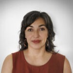 Leslie Roybal is photographed in front of a white background. She is wearing a sleeveless rust-colored top. 