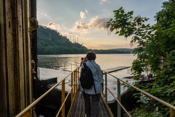 a group of people walk down a metal walkway towards a dock along a river.