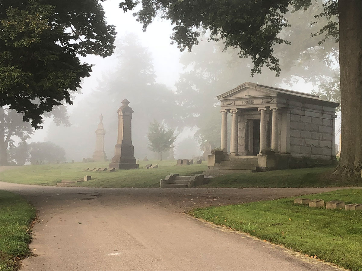 View of Homewood Cemetery. A mausoleum and several other markers are visible through a light fog that hangs in the air.