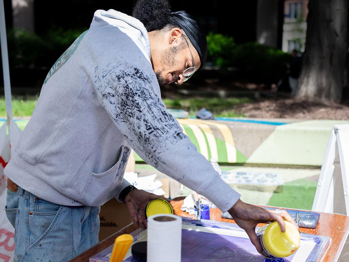 Artist Quaishawn Whitlock pours yellow ink into a frame for silk screening.